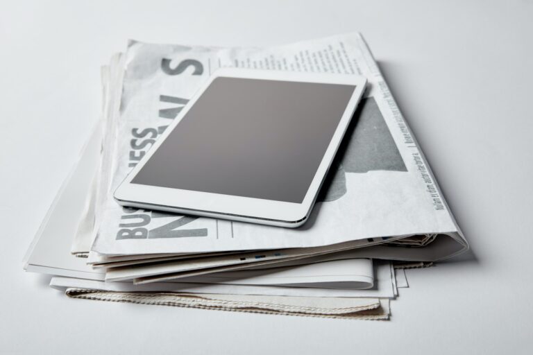 digital tablet with blank screen near business newspapers with articles on white